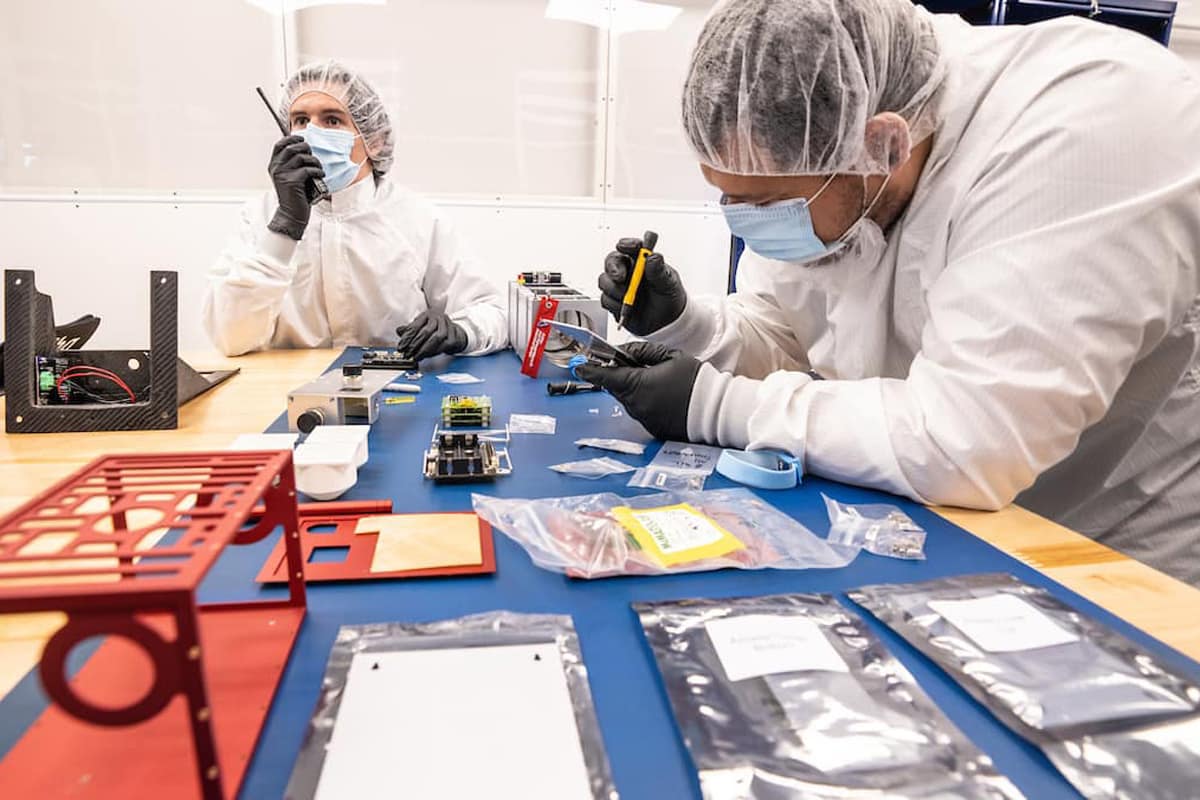 Students in lab coats work on a satellite