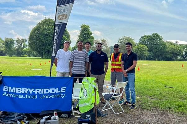 A group of people standing together in front of a drone and a sign which says "Embry-Riddle Aeronautical University".