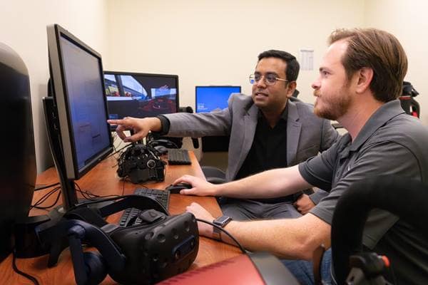 Dr. Subhradeep罗伊(左)和博士.D. student Daniel Lane (right) will utilize VR equipment and an electroencephalogram cap with the driving simulator to better understand automobile driving 行为.