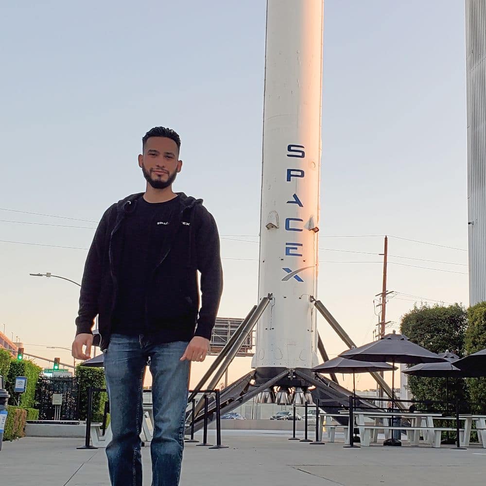 B.S. in Engineering student Marcos Dominguez stands in front of a SpaceX booster.