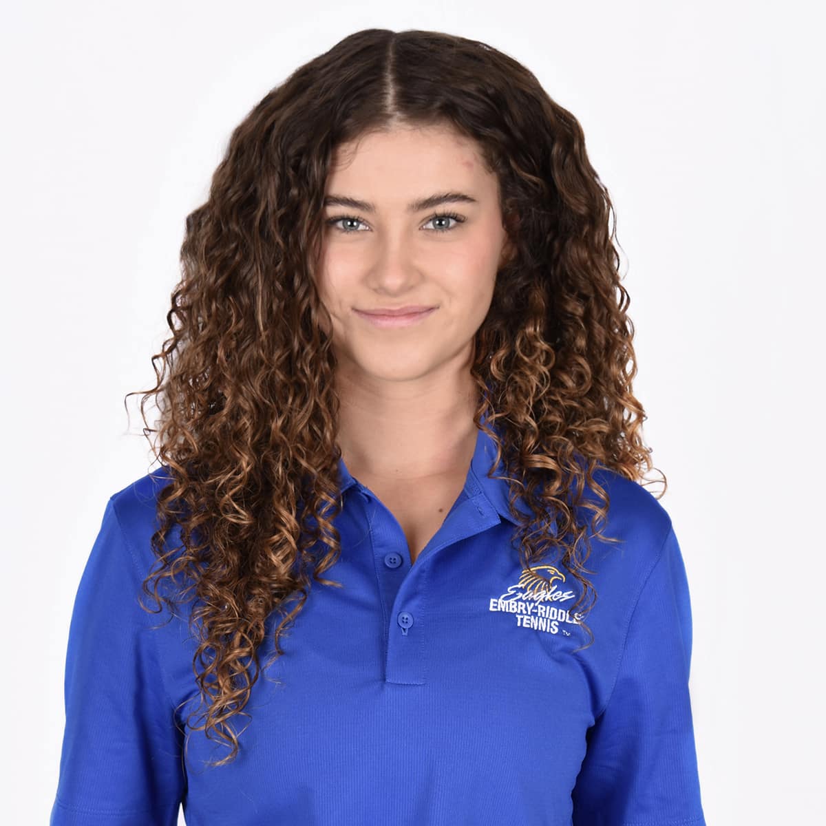 Julia, a white woman with long curly hair, wears a long sleeved blue polo shirt.