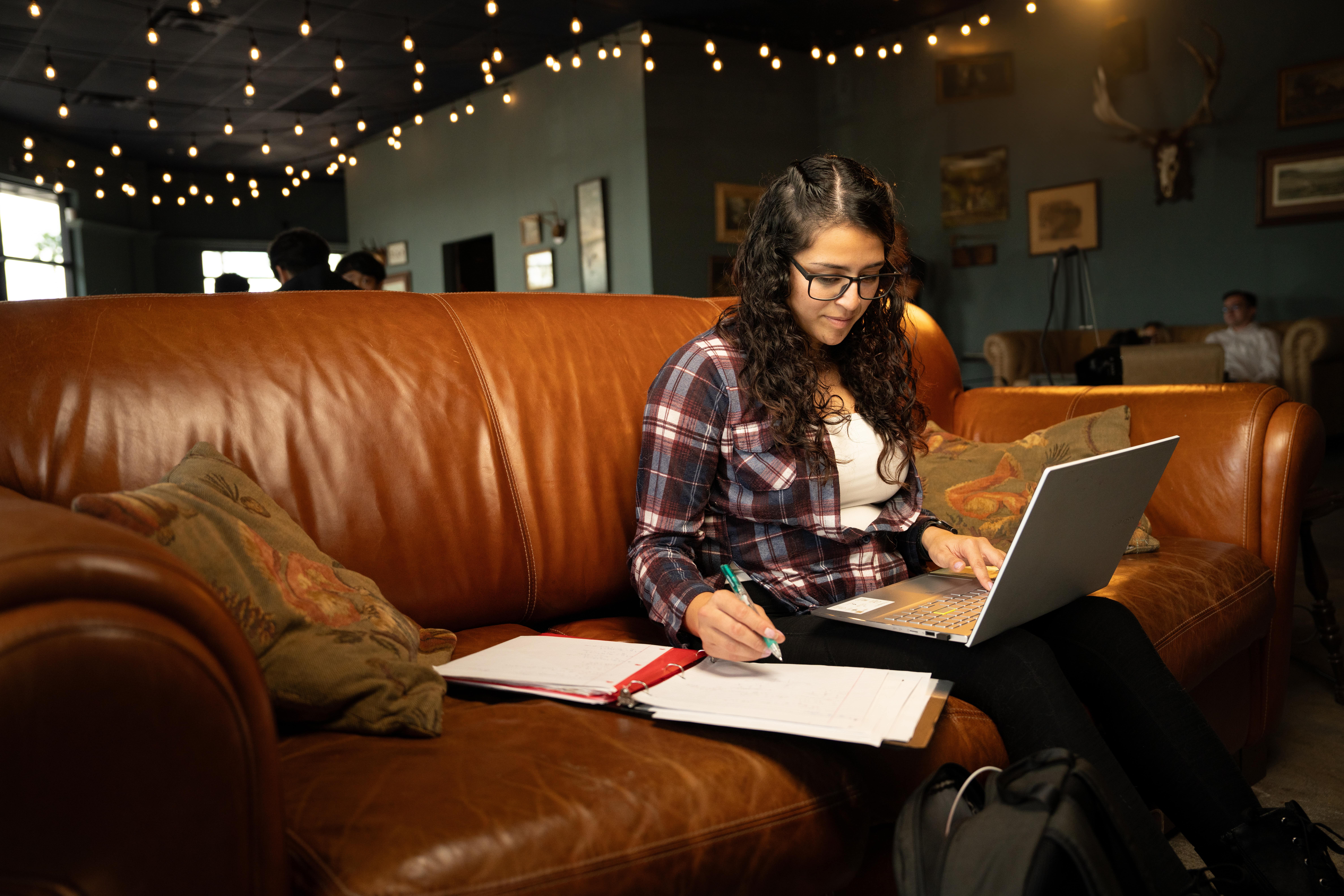 A student sits with a laptop open on her lap, sitting in an overstuffed leather sofa.