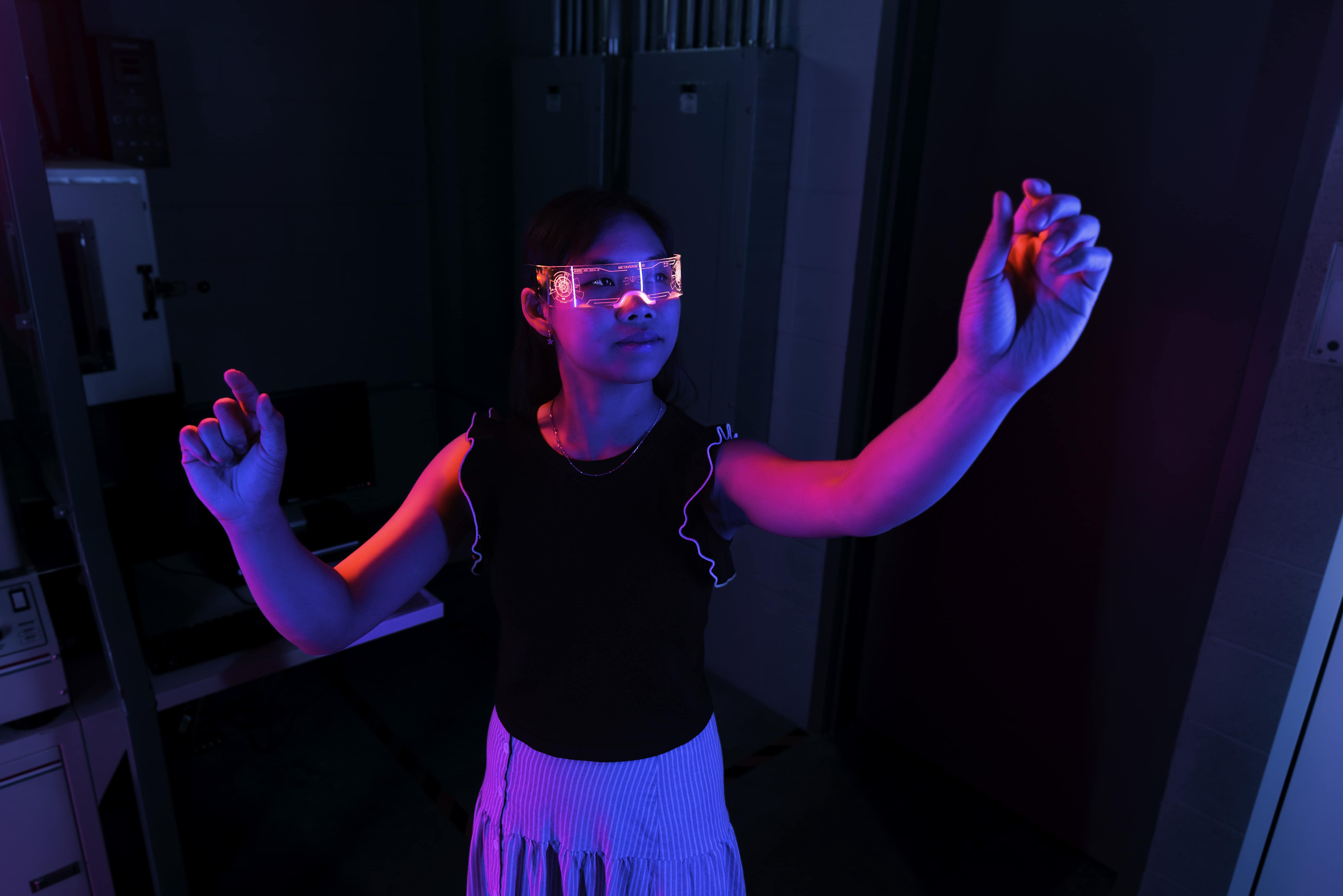 A student wears glowing, transparent goggles and reaches with each hand for a different, invisible instrument.