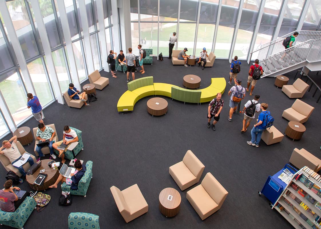 Seen from above, students meet and study in Hunt Library common space, in front of two walls of floor to ceiling windows.