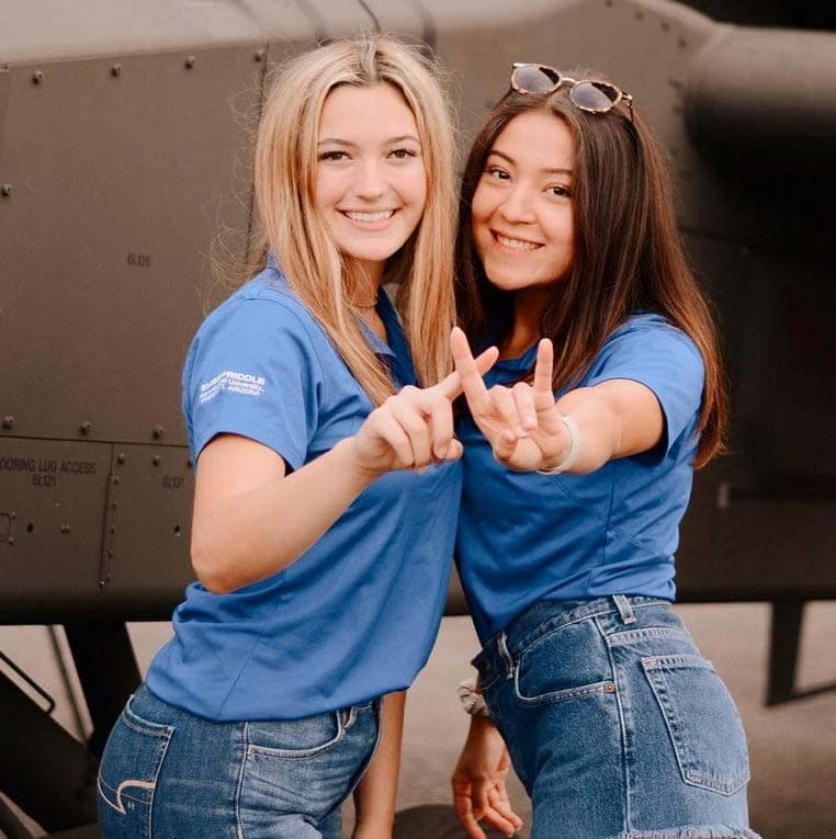 Two female students at an airshow take a picture in front of historical aircraft.