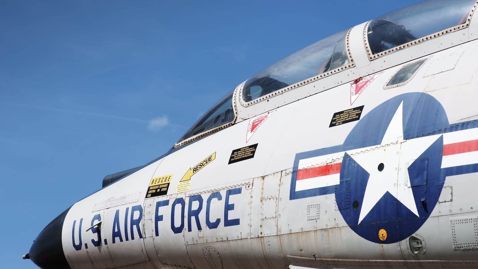 U.S. Air Force jet aircraft cockpit and fuselage with rescue markings and military insignia against a clear blue sky.