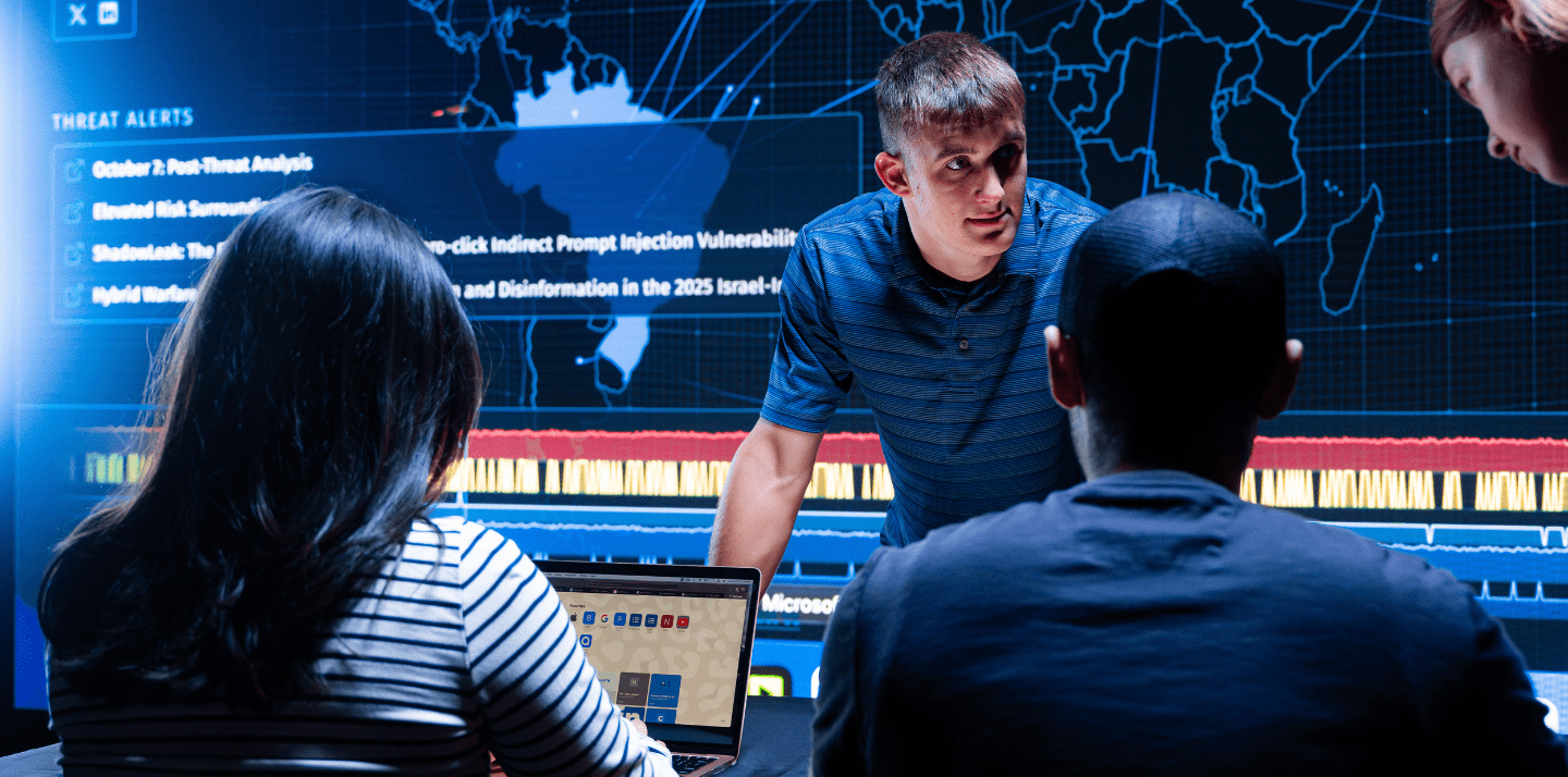 Students collaborate in a cybersecurity operations lab reviewing threat alerts and global attack data displayed on a large interactive world map dashboard.