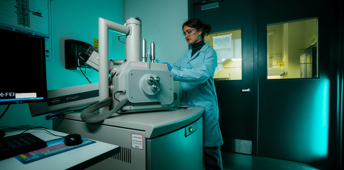 Researcher in a lab coat operating a large electron microscope in a laboratory.