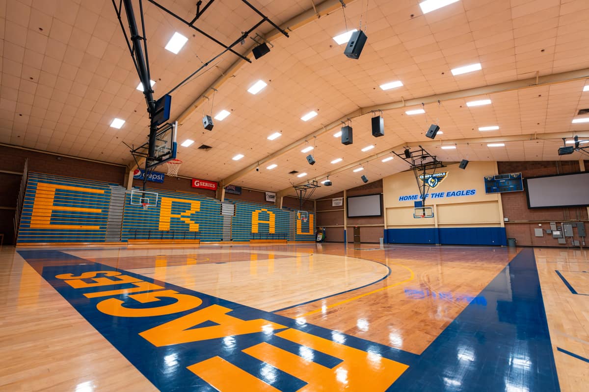 Inside a gymnasium with blue, orange, and light brown floors, with the lights on.