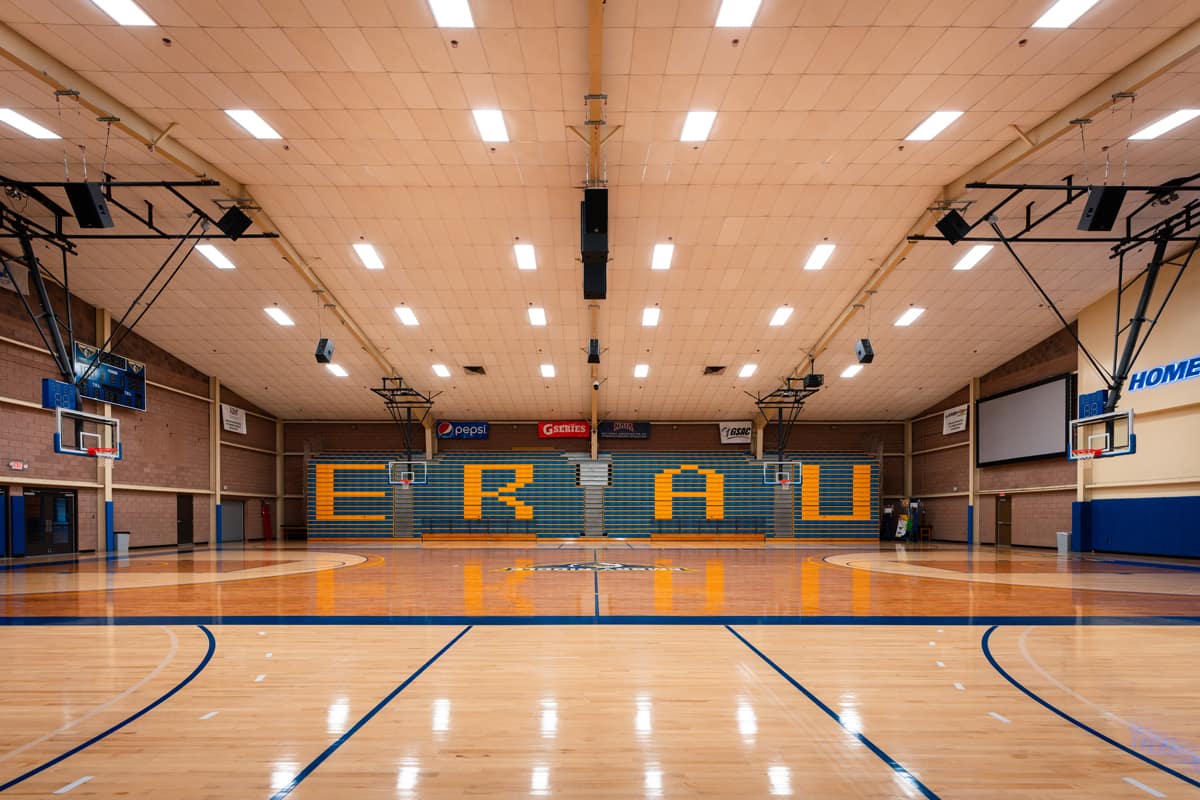 A front view inside a gymnasium with the lights on, showing letters on the wall that spell “ERAU.”