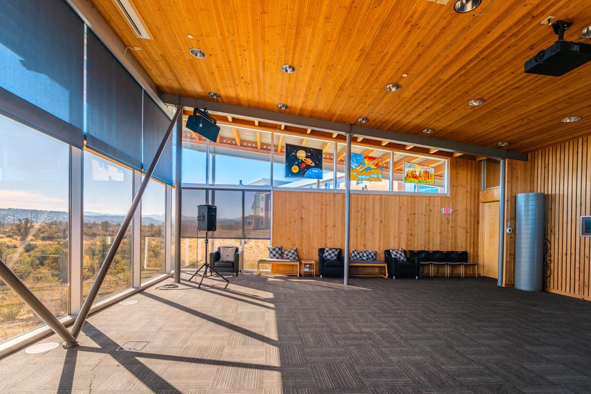 A side view of a large indoor room with a high wooden ceiling and floor-to-ceiling windows letting in natural light.