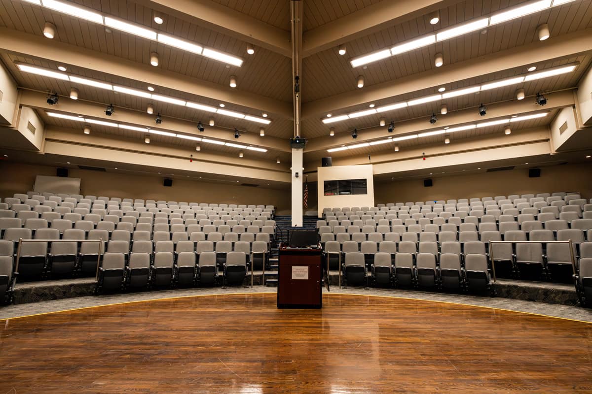 A stage-level view facing the seating area of an empty auditorium, with rows of chairs where an audience would normally be seated.