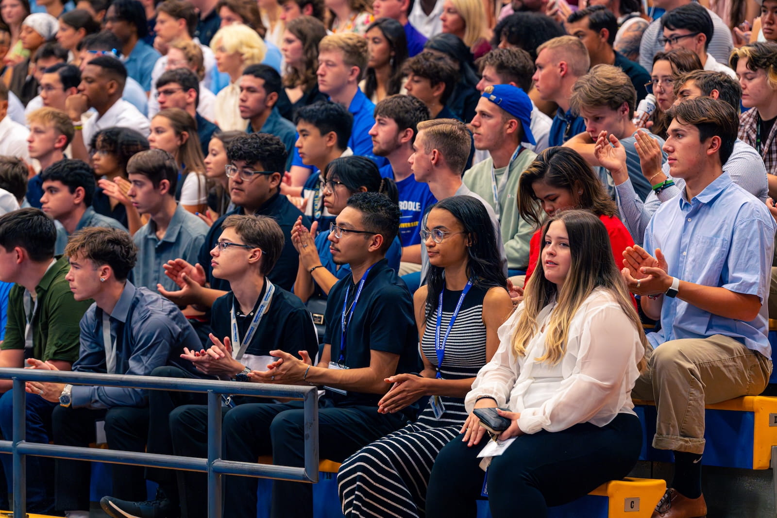 Students seated in bleachers in the audience applaud during convocation.