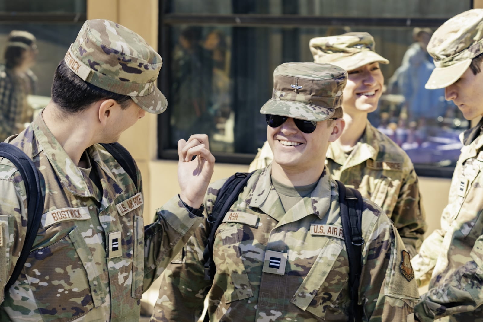 Four U.S. Air Force cadets in camouflage uniforms stand together outdoors, smiling and talking.