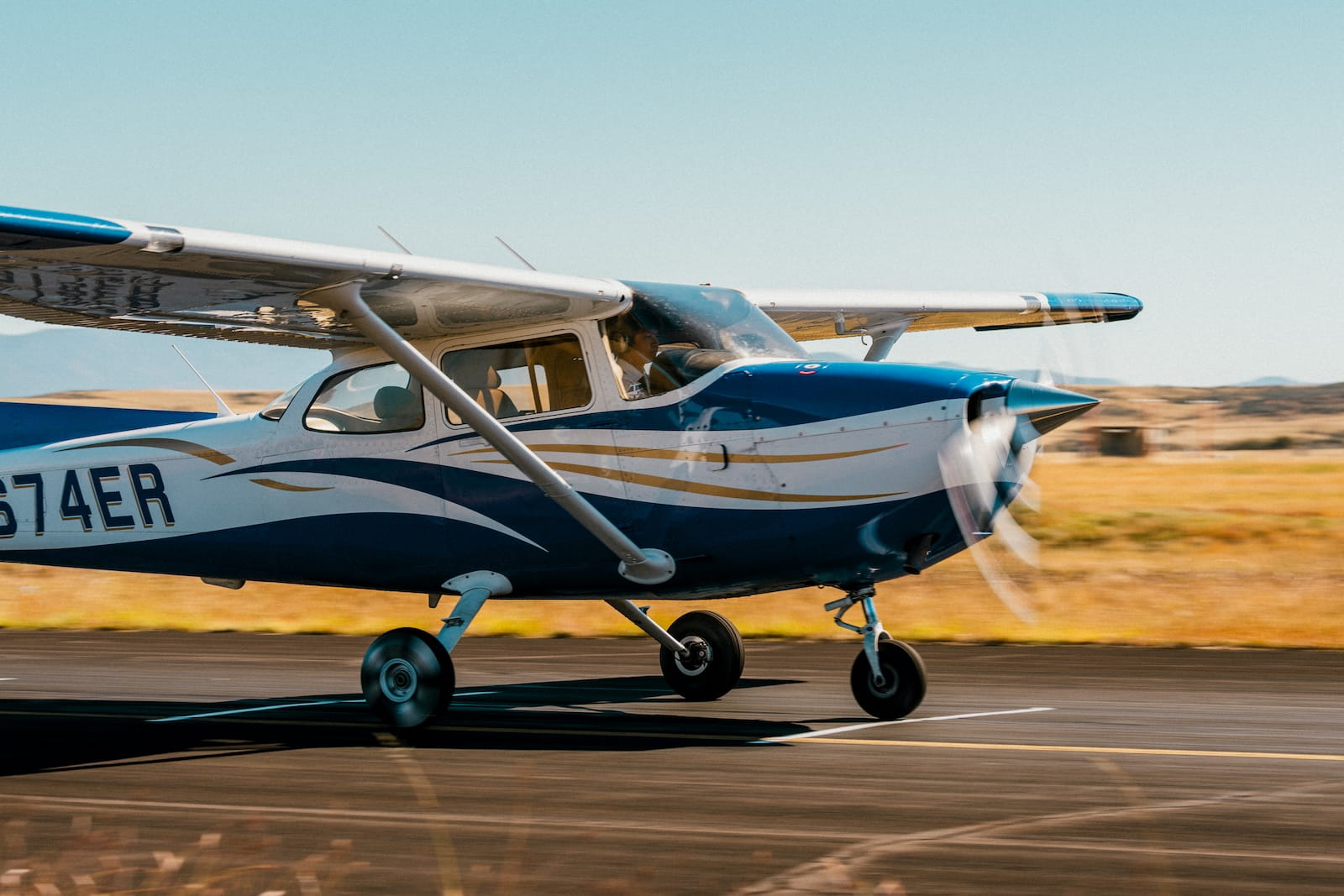 Single-engine high-wing training aircraft with tricycle landing gear and spinning propeller accelerating on runway.