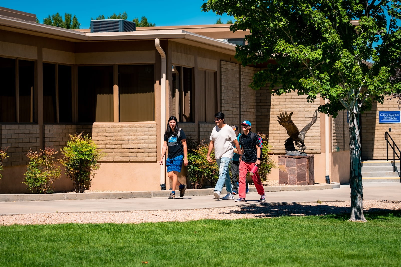 Students walk past a campus building and an eagle statue on a sunny day at Embry-Riddle’s Prescott campus.