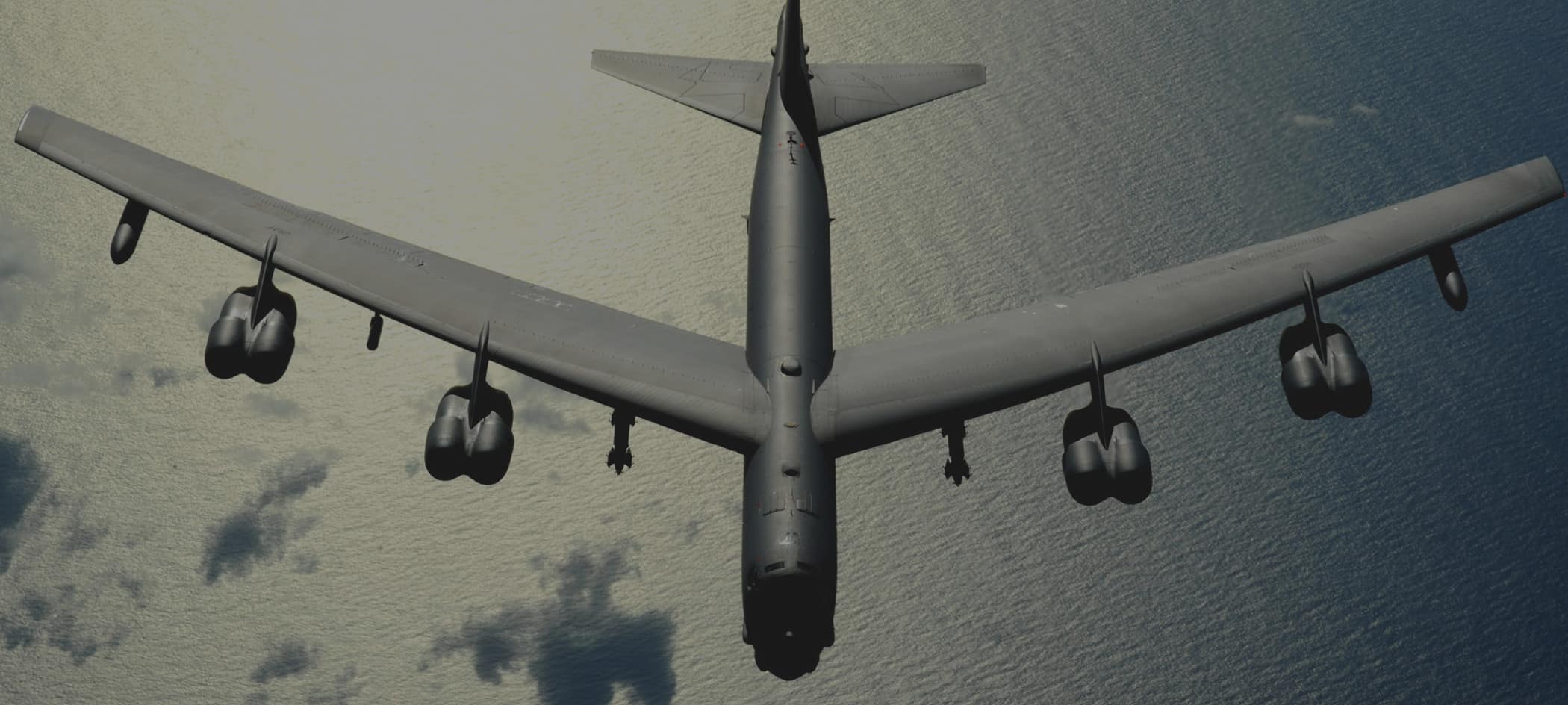 Overhead view of a military plane flying over a body of water.
