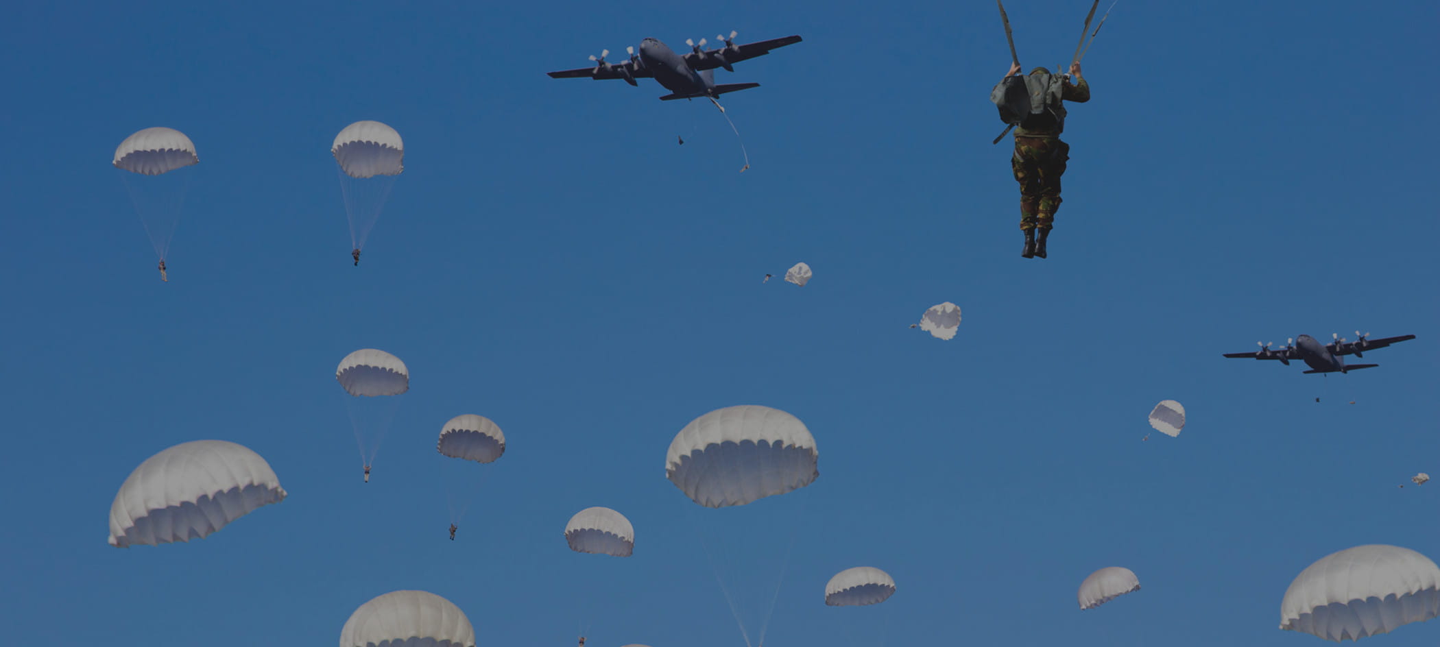 Parachutes fall from sky while planes fly above.