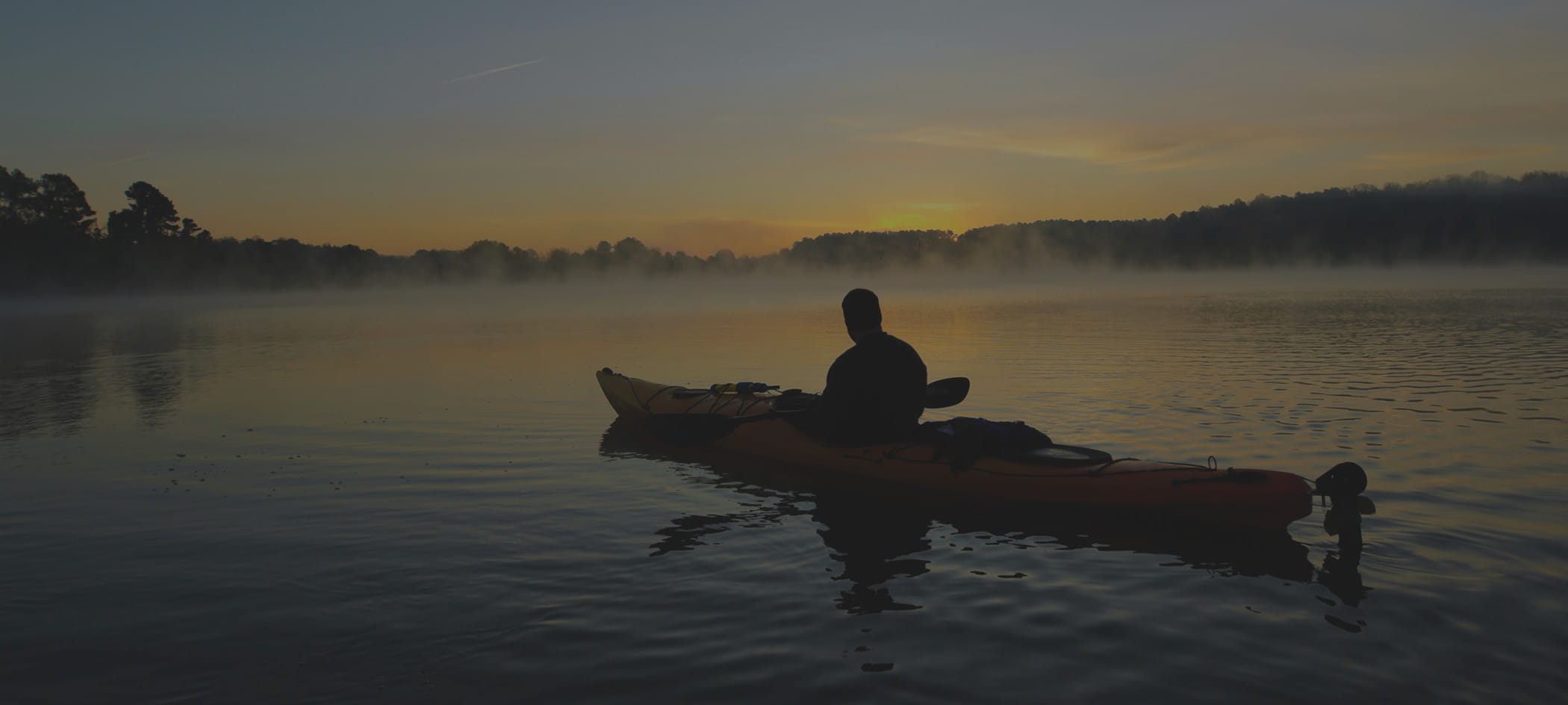 Person rides in kayak on lake at sunset.