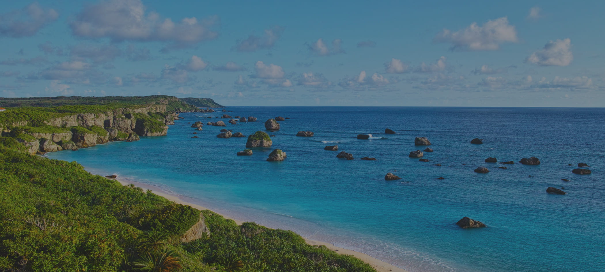 A coastline with rocks rising from the ocean with a blue sky in the background.