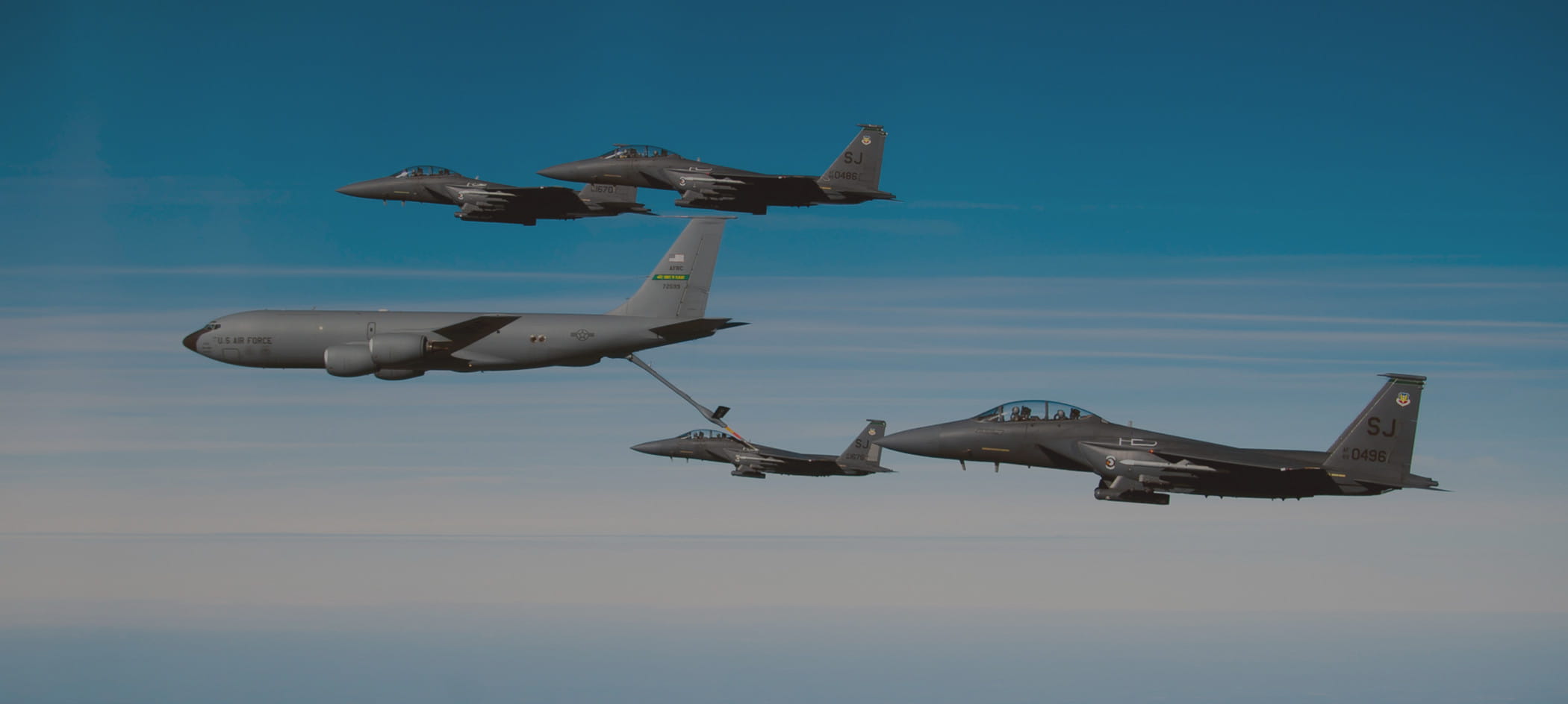 Four jets surround cargo plane in blue sky.