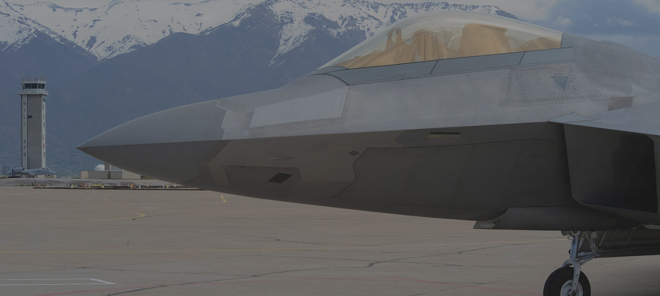 Front of fighter jet with mountains in background.