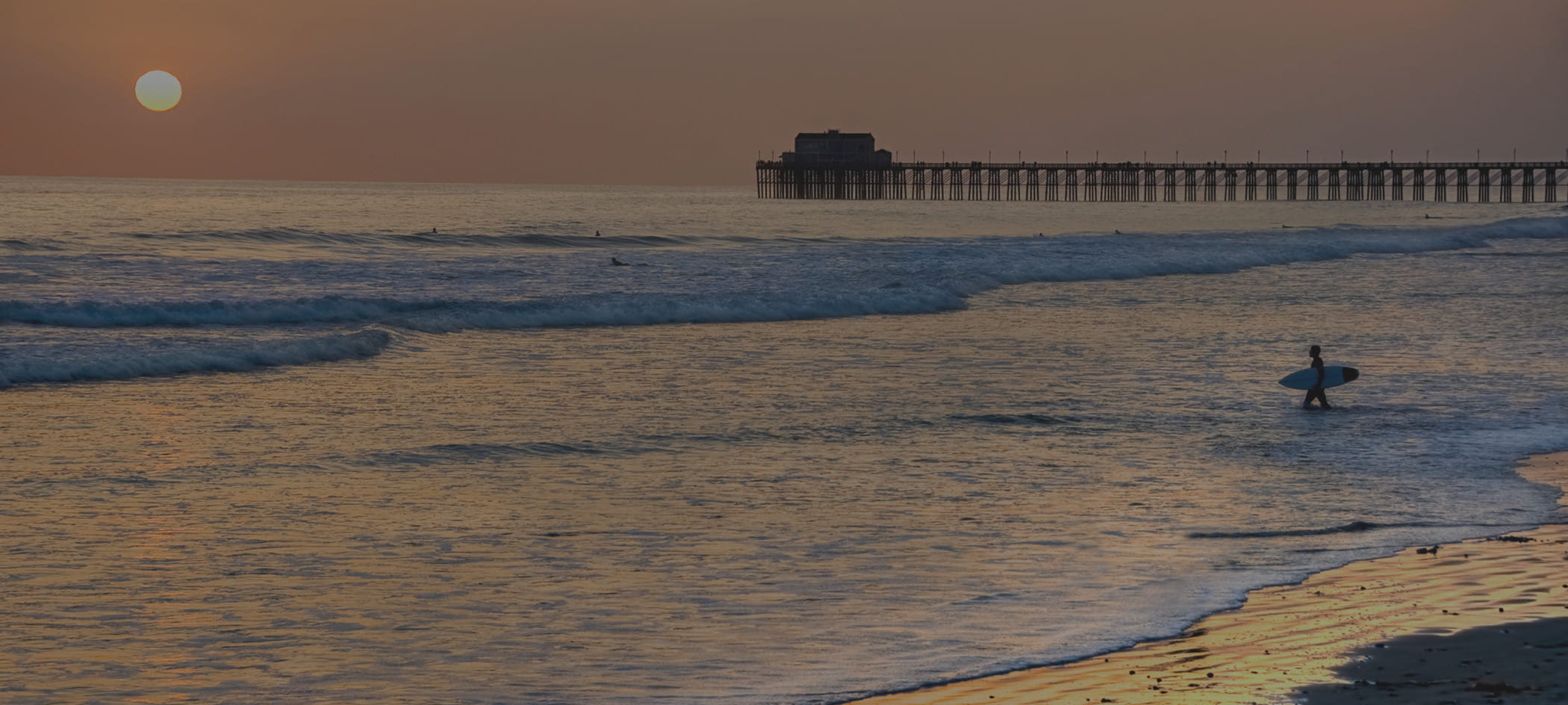 Waves crash on shore during sunset.