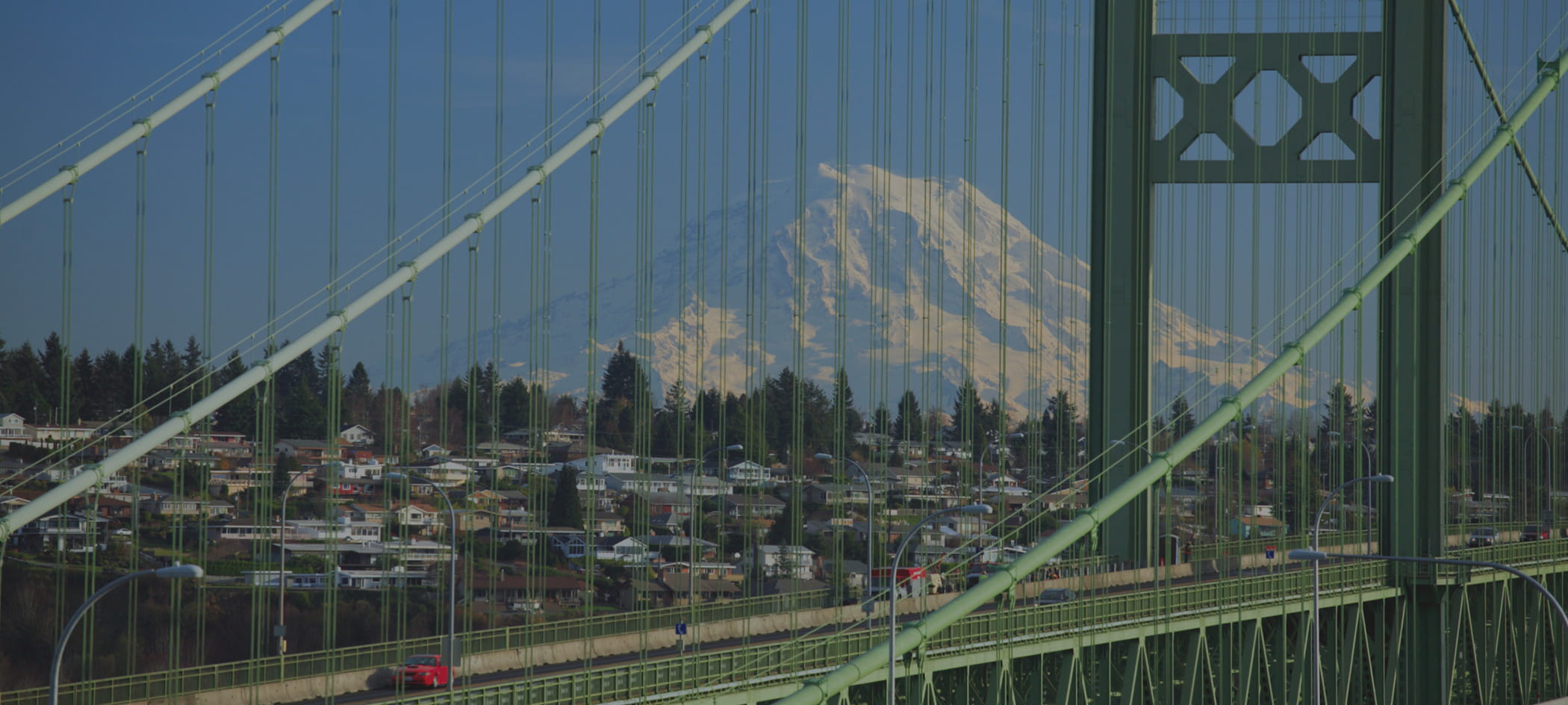 A green suspension bridge with cars driving on it.