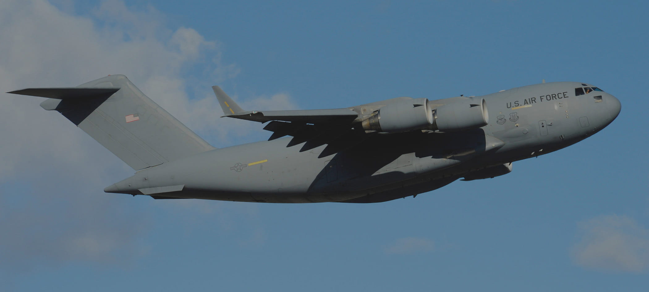 Military cargo plane flies in blue sky.