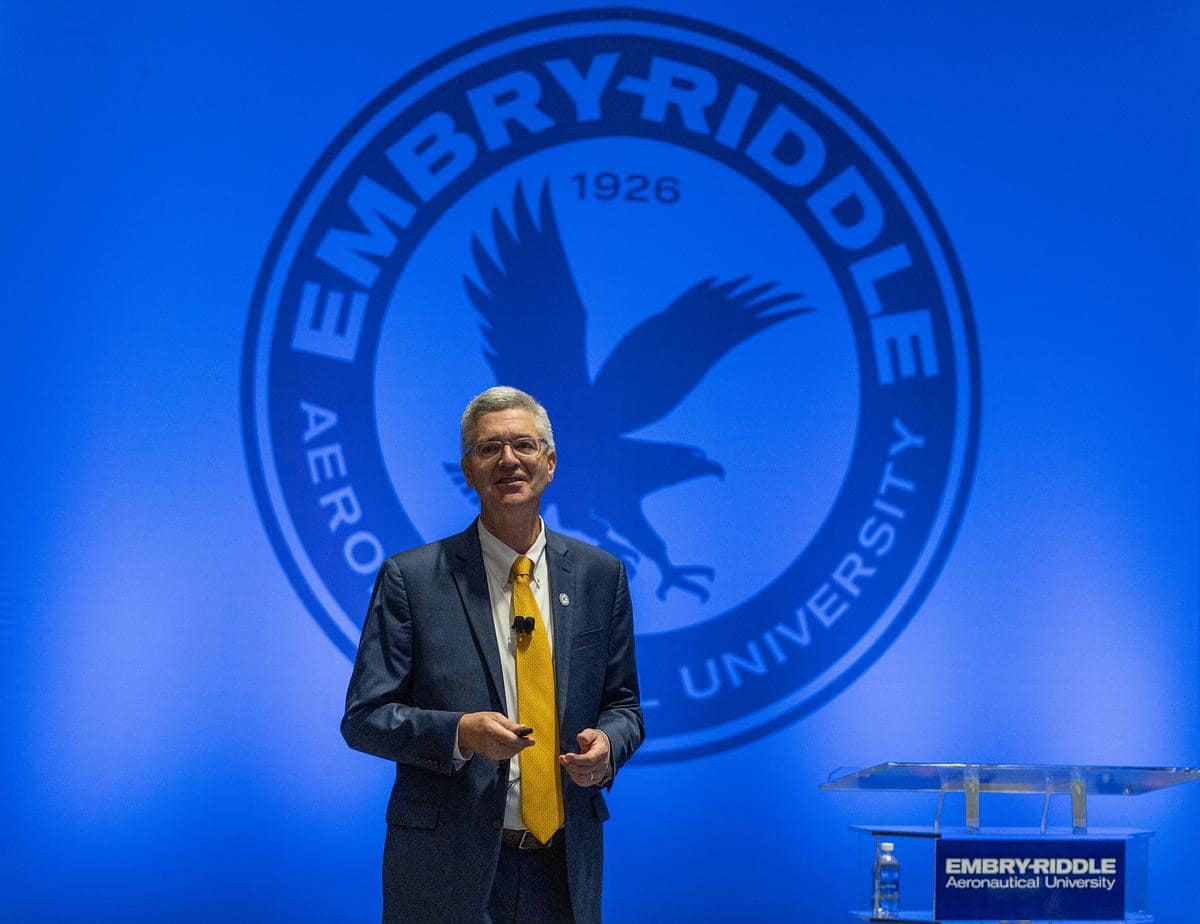 Dr. Butler speaks on stage in front of a large Embry-Riddle Aeronautical University seal and podium, during a formal presentation event.