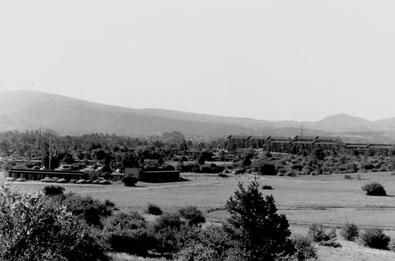Early view of Embry-Riddle Prescott Campus with low buildings, airfield, and surrounding desert landscape with Granite Mountain in background, black and white photo.