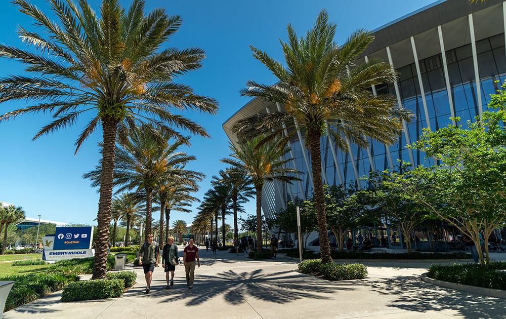 Students walk along a palm-lined campus walkway beside Daytona Beach student union on a sunny day.