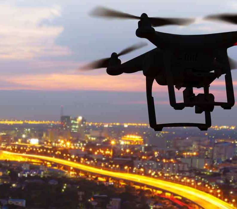 A drone flies above a city at sunset