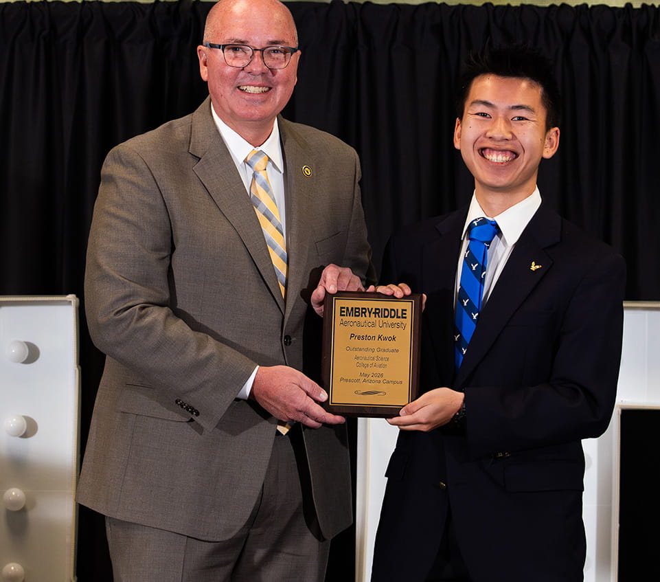 Two men in suits holding award plaque reading Embry-Riddle Aeronautical University, Preston Kwok, Outstanding Graduate, Aeronautical Science, College of Aviation, May 2026, Prescott, Arizona Campus, smiling in front of stage backdrop.