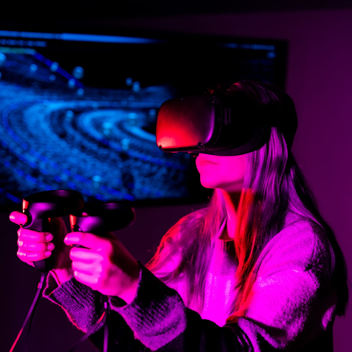 Student using virtual reality headset and handheld controllers with space simulation displayed on screen behind.