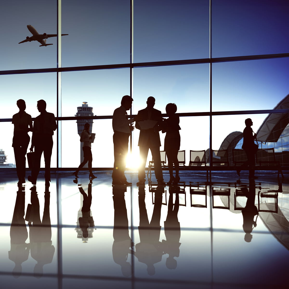 Silhouetted travelers standing in airport terminal near large windows with aircraft taking off outside.