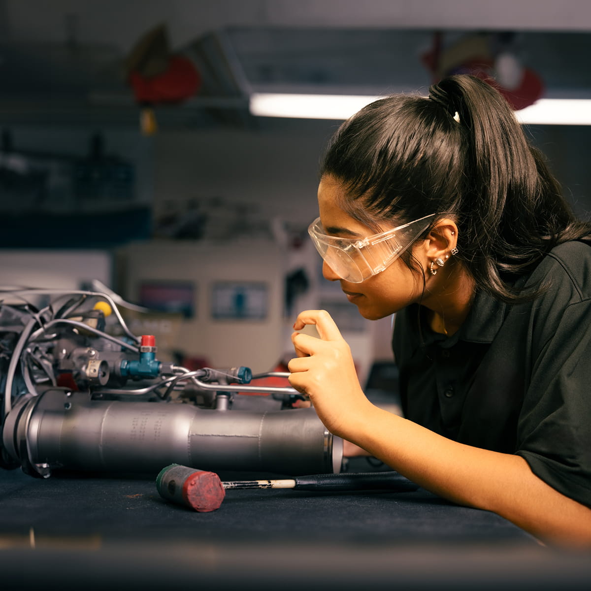 Student using precision tool to work on mechanical assembly with exposed wiring and components in lab.