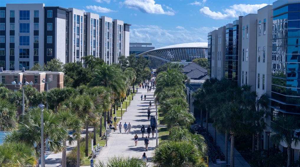An elevated view of the Daytona Beach campus, showing buildings, palm trees, and students moving through the walkways.
