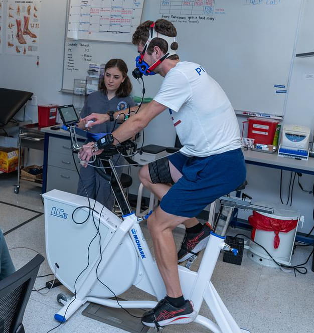 Man rides an exercise bike while a researcher looks on.