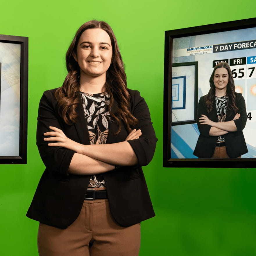 Jillian Preite stands in front of a green screen with a monitor to her side, showing her in front of a weather forecast