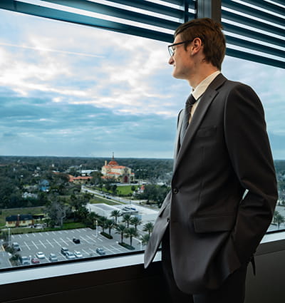 Embry-Riddle student in professional dress stands looking out a window