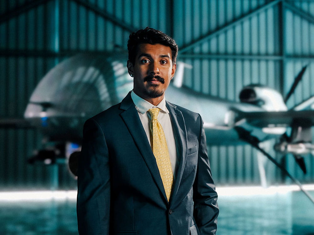 A student in a suit stands in front of an airplane in a hangar