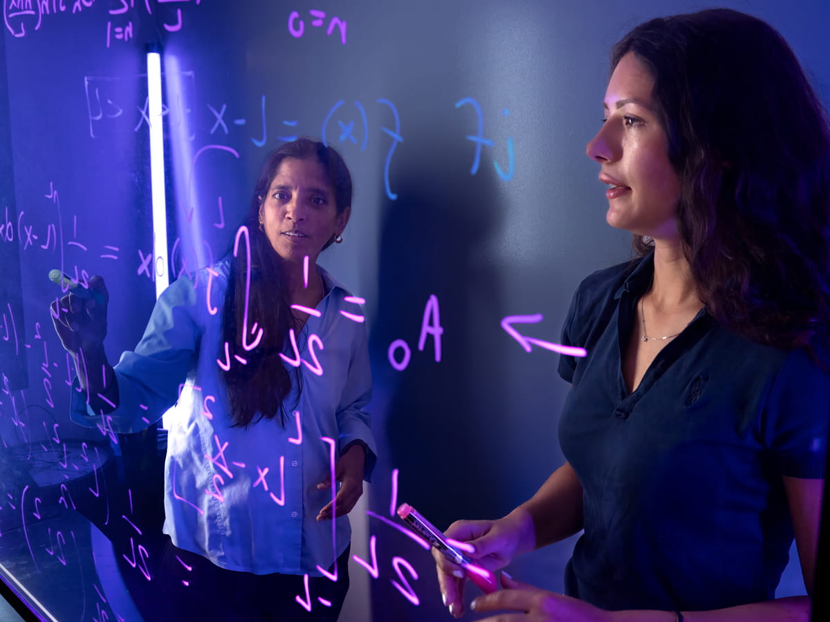 Women work on a formula on a marker board.