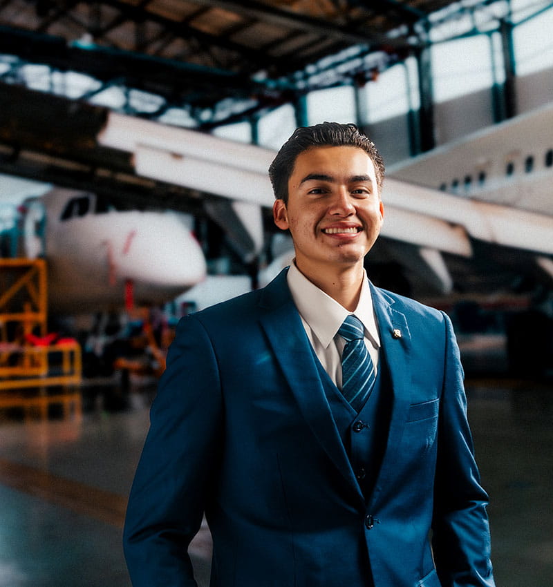 Student wearing a suit stands in a hangar in front of two planes