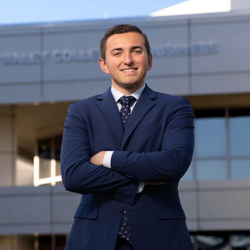 Tyler DeZell stands in a suit in front of the Daytona Beach College of Business