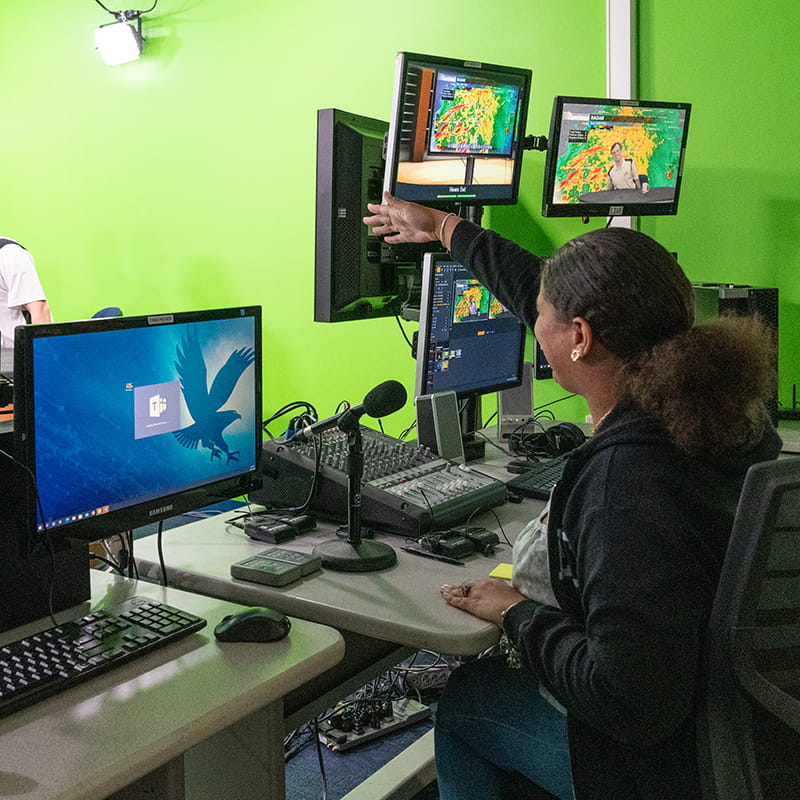 Embry-Riddle student sits at a computer controlling the graphics and camera during a weather broadcast