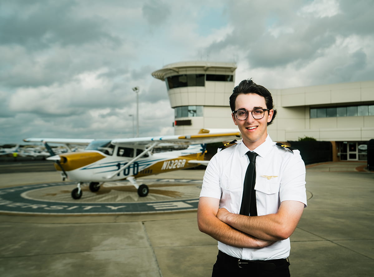 An Embry-Riddle student stands outside on the tarmac near a small plane