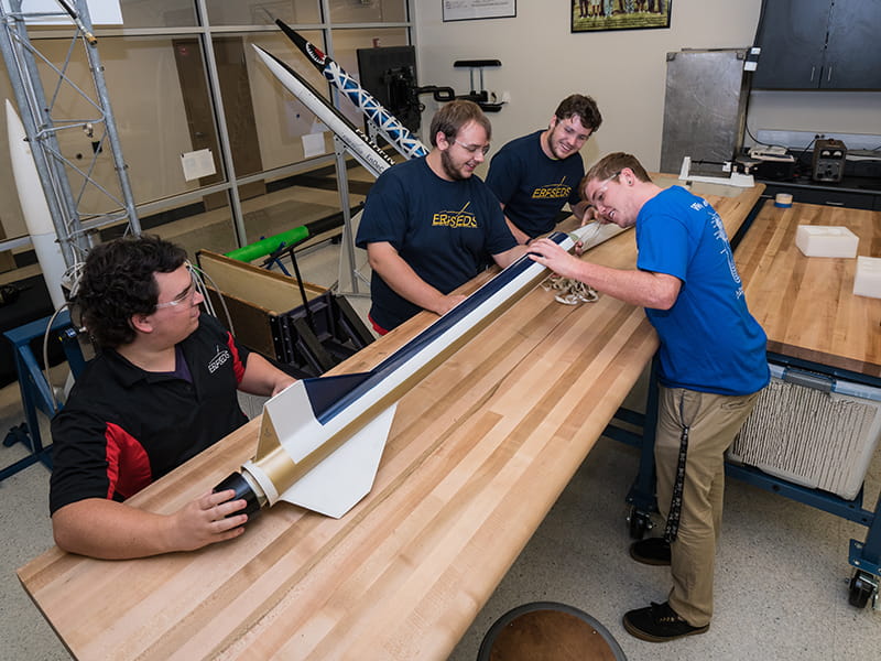 Embry-Riddle students work on a rocket on a table in a lab on the Daytona Beach Campus