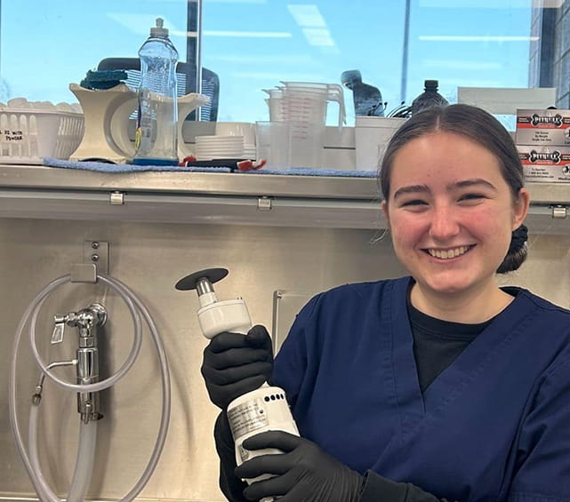 Embry-Riddle student stands in an autopsy lab and holds a piece of equipment