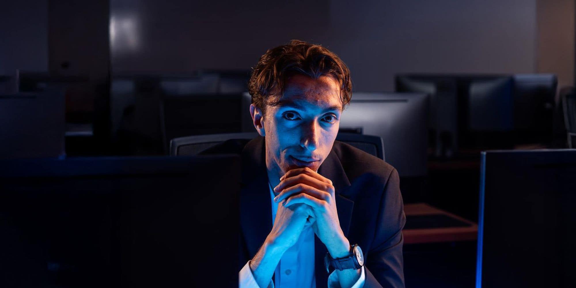 Student sits with his hands folded beneath his chin under a blue glow.